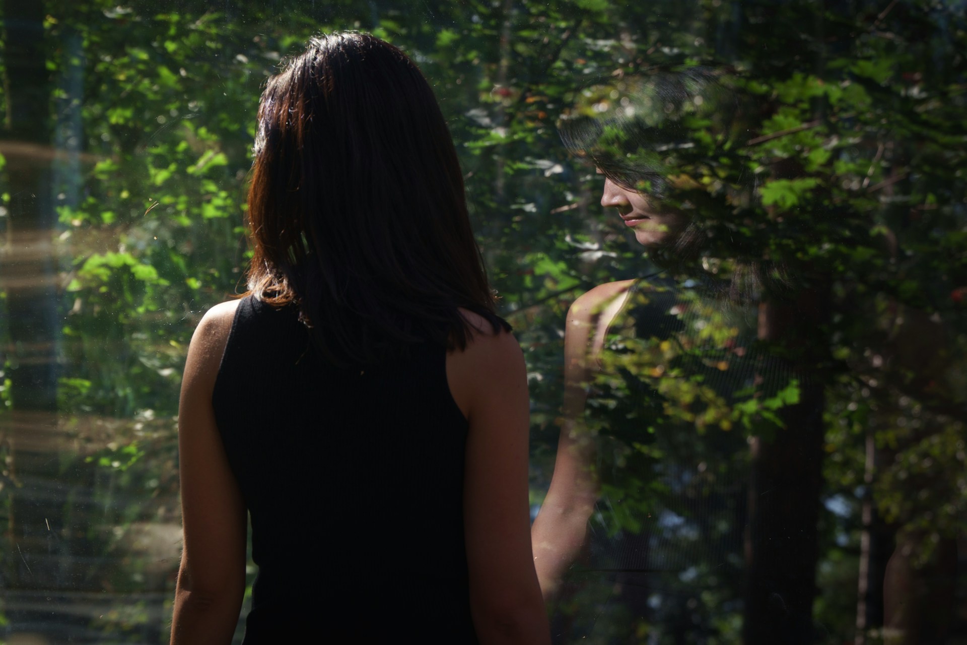 Woman looking out a window, reflecting among trees